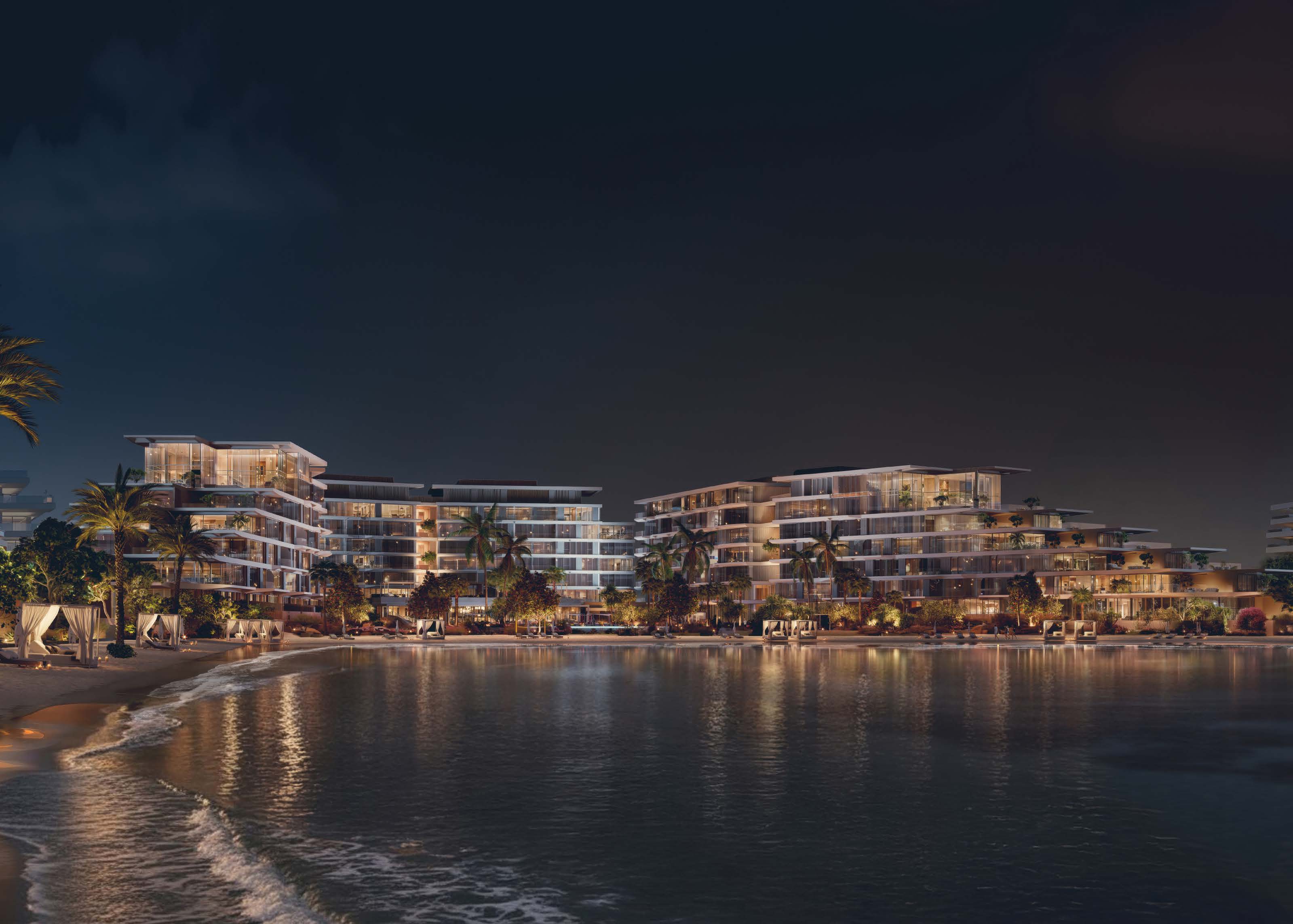 The buildings lit at night, reflected in the water off the private beach